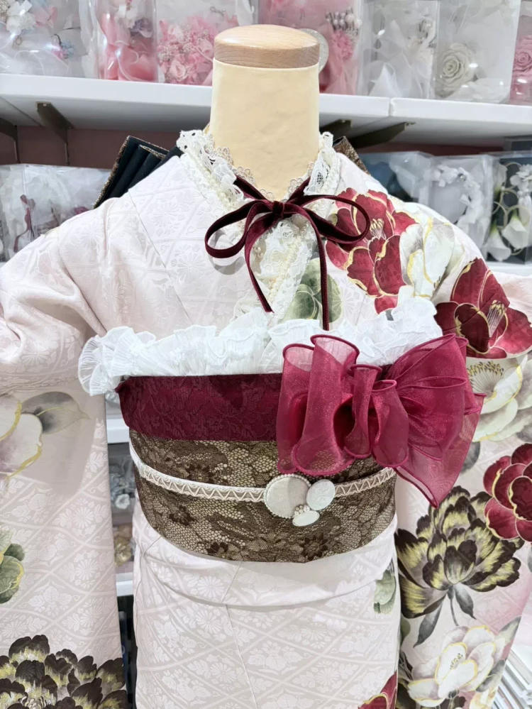 TKAZEN姫路店で人気のレトロ可愛い椿柄の振袖コーディネート。淡いピンクの振袖に赤い椿の花柄が華やかで、姫路の成人式におすすめの振袖スタイル。