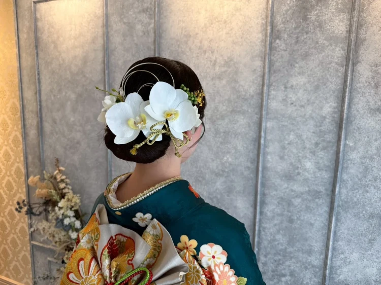白の大きな花飾りを主役にした、低めシニヨンの上品で落ち着いた振袖ヘアアレンジ