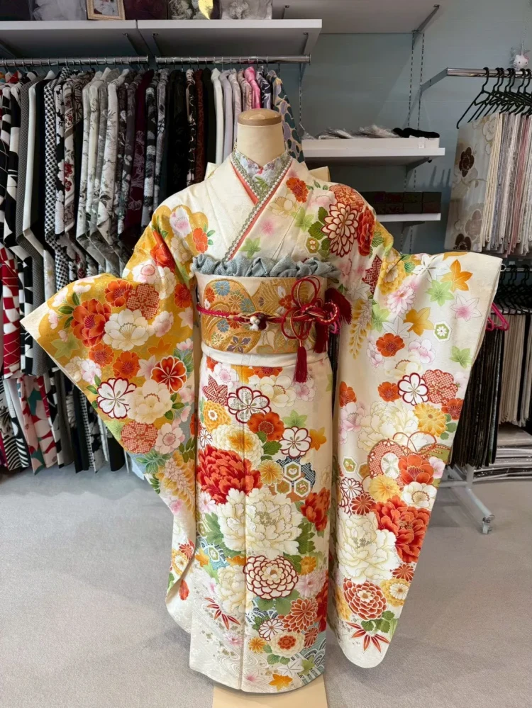 白地に温かみのあるオレンジや黄色、赤の大きな牡丹や菊の花々が豪華に描かれた、タカゼンの上品で華やかな正統派プレミアム古典振袖のトルソー（マネキン）コーディネート写真