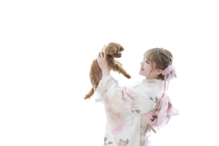 振袖を着た女性が愛犬のトイプードルを抱き上げて見つめ合う前撮り写真。TAKAZEN堺店のペットと一緒に撮影できる成人式前撮りプランのイメージ。 