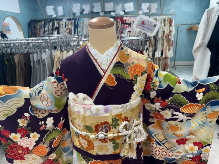 濃紫をベースに牡丹や菊、松、梅などの古典柄が華やかに描かれた振袖コーディネート。ゴールドの帯と白系小物を合わせた豪華で上品な成人式向けスタイル