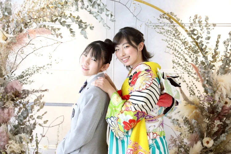華やかな黄色の振袖姿のお嬢様と、制服姿のご家族が並んだ姉妹写真。仲良く寄り添った自然な表情が魅力的な記念写真。