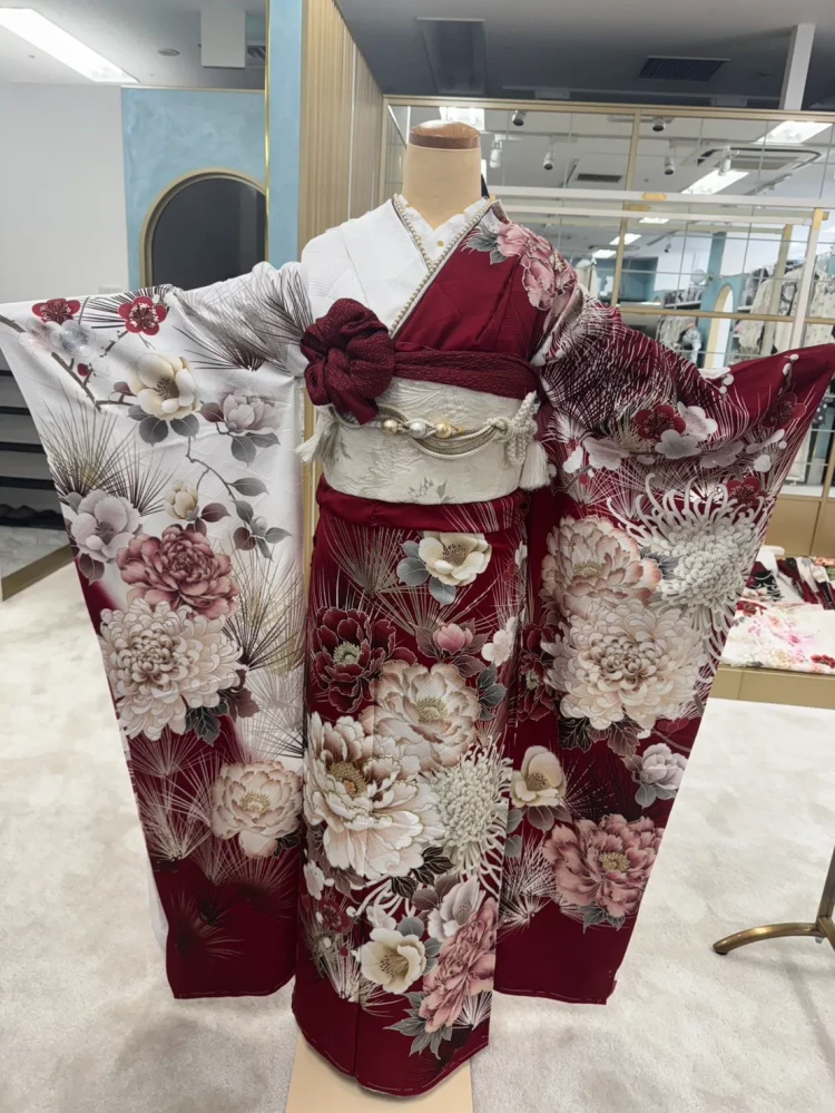 深いボルドー色に白やピンクの花々が映える、華やかな古典柄の振袖。松や菊、ボタンなどの花柄が全体にあしらわれ、白地の袖とのコントラストが印象的なコーディネート