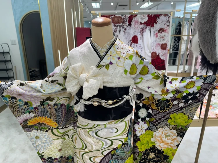 白地に黒・緑・紫の花柄が映える華やかな振袖コーデ。大きな花模様と扇柄が印象的で、黒の帯と白の小物を合わせた大人っぽく個性的なスタイル。