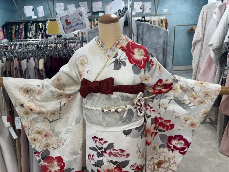 白地に赤と淡いピンクの花柄が華やかに描かれた振袖のコーディネート。シルバーの帯にボルドーのリボンを合わせた上品な成人式スタイル